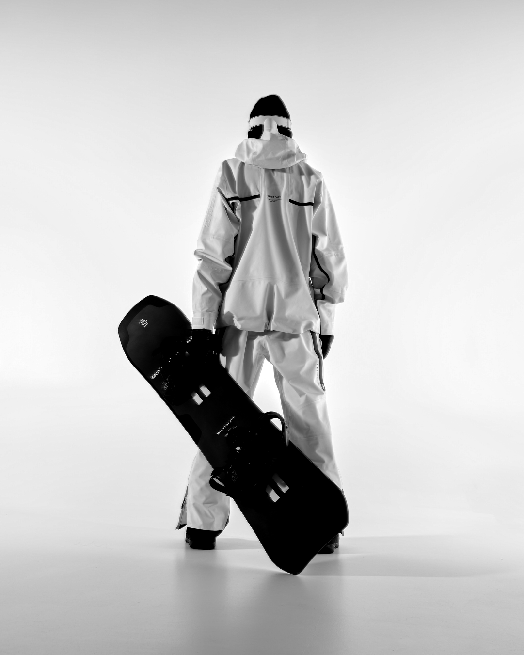 Person wearing 3L Performance 3-In-1 Jacket in warm White and Black facing away from the camera holding the Moncler Grenoble x WHITESPACE Snowboard.