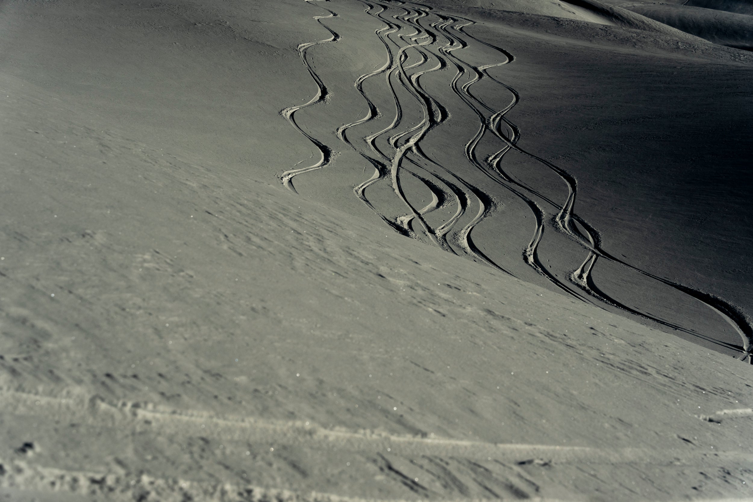 Low angle of a snowy mountain base with wavy snowboard and ski tracks criss crossing each other down the mountain.
