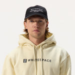 Man wearing a cream 'WHITESPACE' hoodie and dad hat in black on a white background.