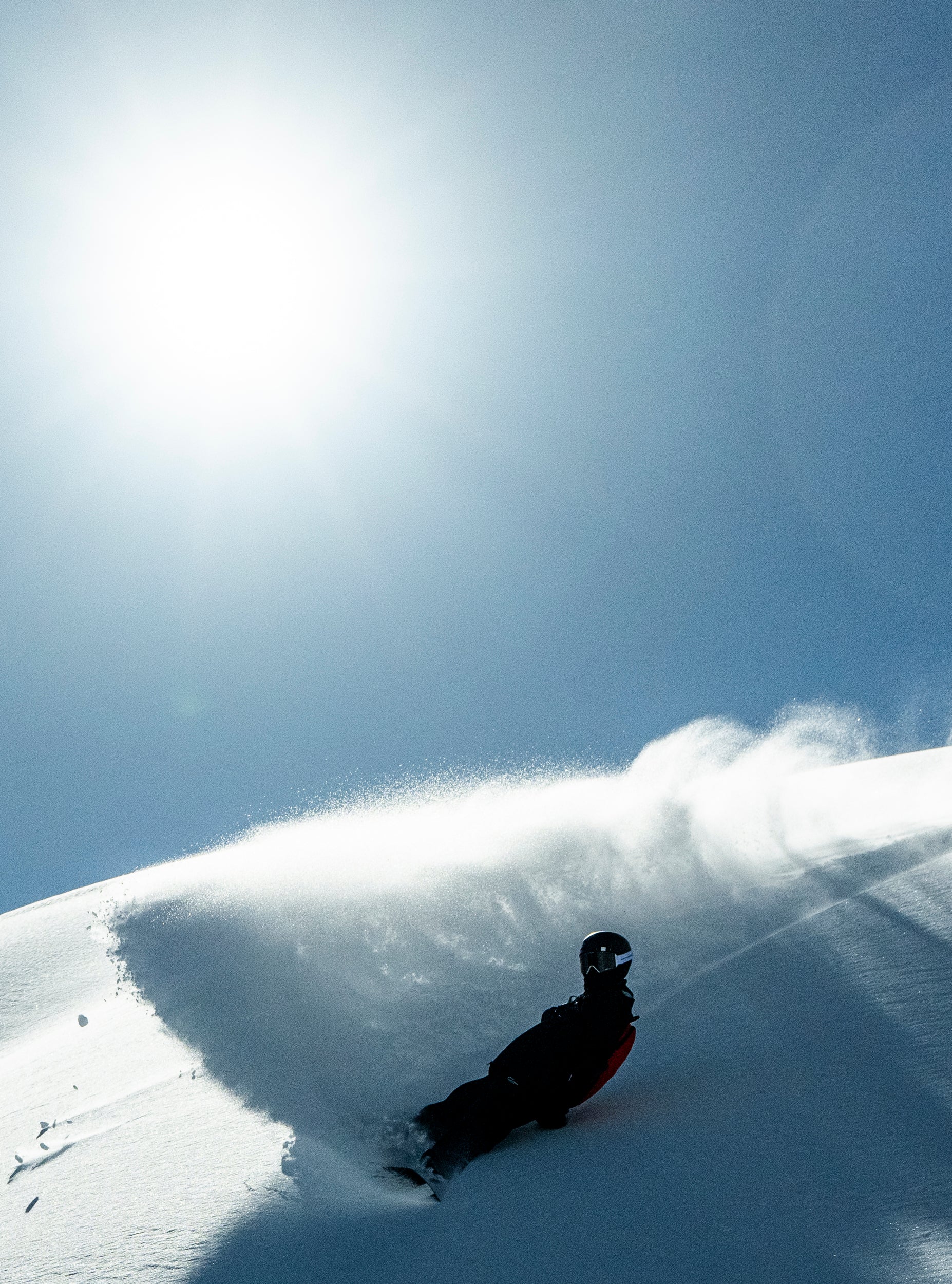 Person snowboarding down a snowy mountain with snow spraying from carving into the snow. 
