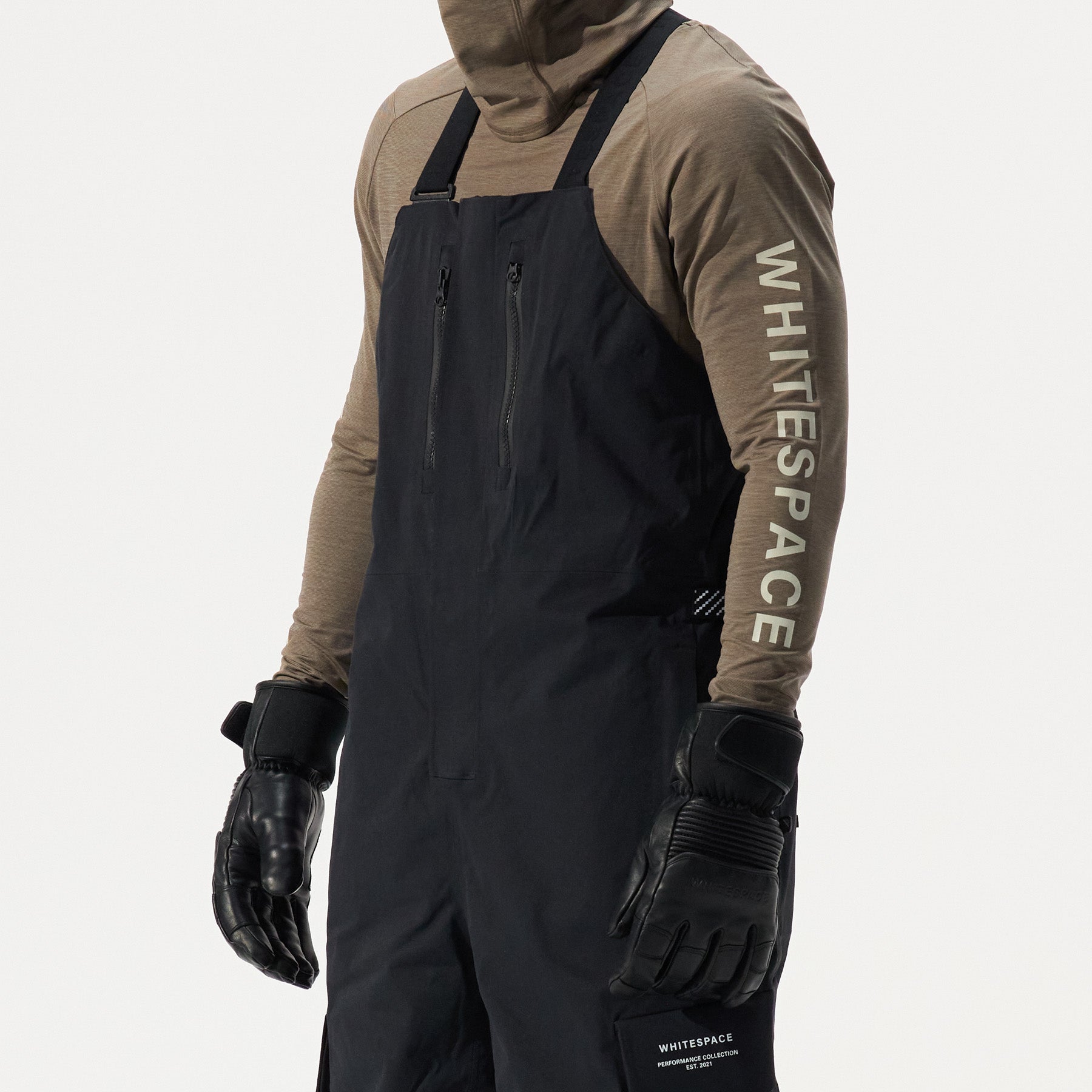 Model wearing black bib overalls with brown long sleeves and 'Whitespace' branding on a white background