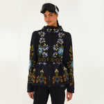 Model wearing Farm Rio Garden belted jacket, a black jacket with blue, orange and white flower design, black ski goggles, and black pants, on a white background.