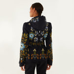 Model, from the back, wearing Farm Rio Garden belted jacket, a black jacket with blue, orange and white flower design, and black pants, on a white background.