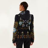 Model, from the back, wearing Farm Rio Garden belted jacket, a black jacket with blue, orange and white flower design, and black pants, on a white background.