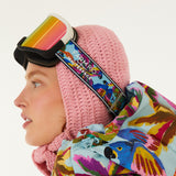 Head shot of model looking left, wearing Farm Rio/WHITESPACE ski googles over a crochet hood and light blue puffer jacket with macaw graphics, on a white background.