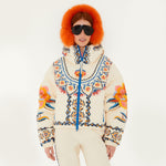 Model wearing Farm Rio Lucy Floral Puffer Jacket, a cream colored jacket with blue and yellow floral designs, coordinating pants, dark sunglasses, and fluffy orange ear muffs, on a white background.