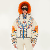 Model wearing Farm Rio Lucy Floral Puffer Jacket, a cream colored jacket with blue and yellow floral designs, coordinating pants, dark sunglasses, and fluffy orange ear muffs, on a white background.