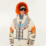 Model wearing Farm Rio Lucy Floral Puffer Jacket, a cream colored jacket with blue and yellow floral designs, coordinating pants, dark sunglasses, and fluffy orange ear muffs, on a white background.