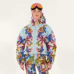 Model wearing Farm Rio Macaw puffer jacket, a light blue jacket with macaw graphic design, matching pants, pink and orange ski goggles, and a crochet hood, on a white background.
