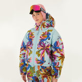 Model wearing Farm Rio Macaw puffer jacket, a light blue jacket with macaw graphic design, matching pants, pink and orange ski goggles, and a crochet hood, on a white background.