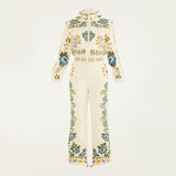Flat lay of Farm Rio Winter Garden jumpsuit, a cream jumpsuit with green and yellow floral designs, on a white background.