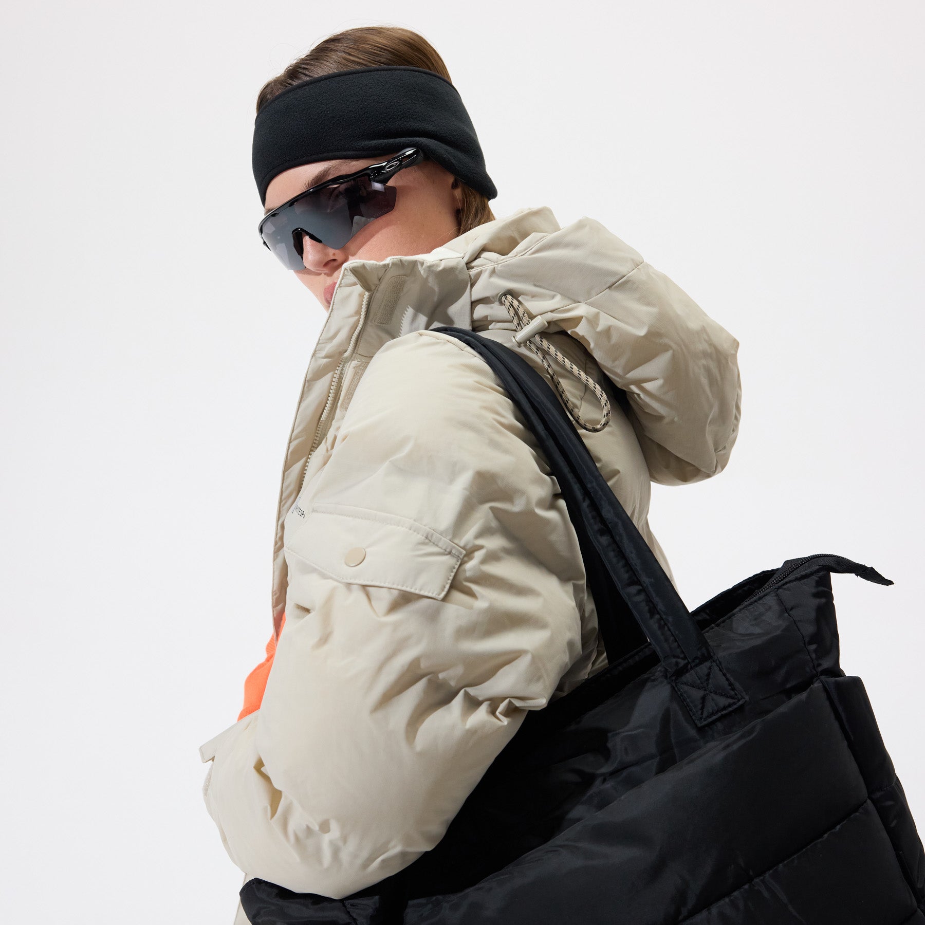 Model wearing a Insulated Parka Jacket in Plaza Taupe, shown from the side, with a large black bag over her shoulder, on a white background.