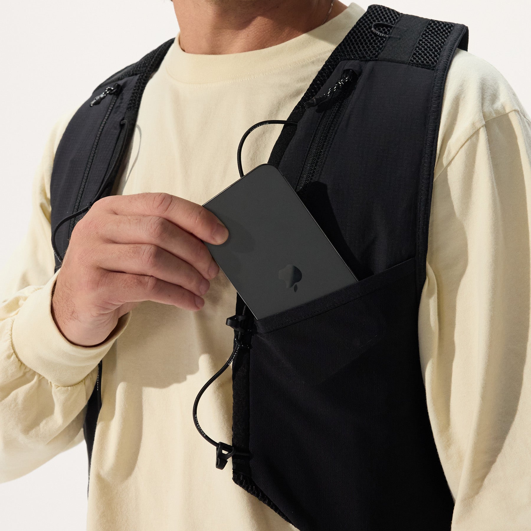 Model storing phone in the chest pocket of black cargo vest, on a white background.