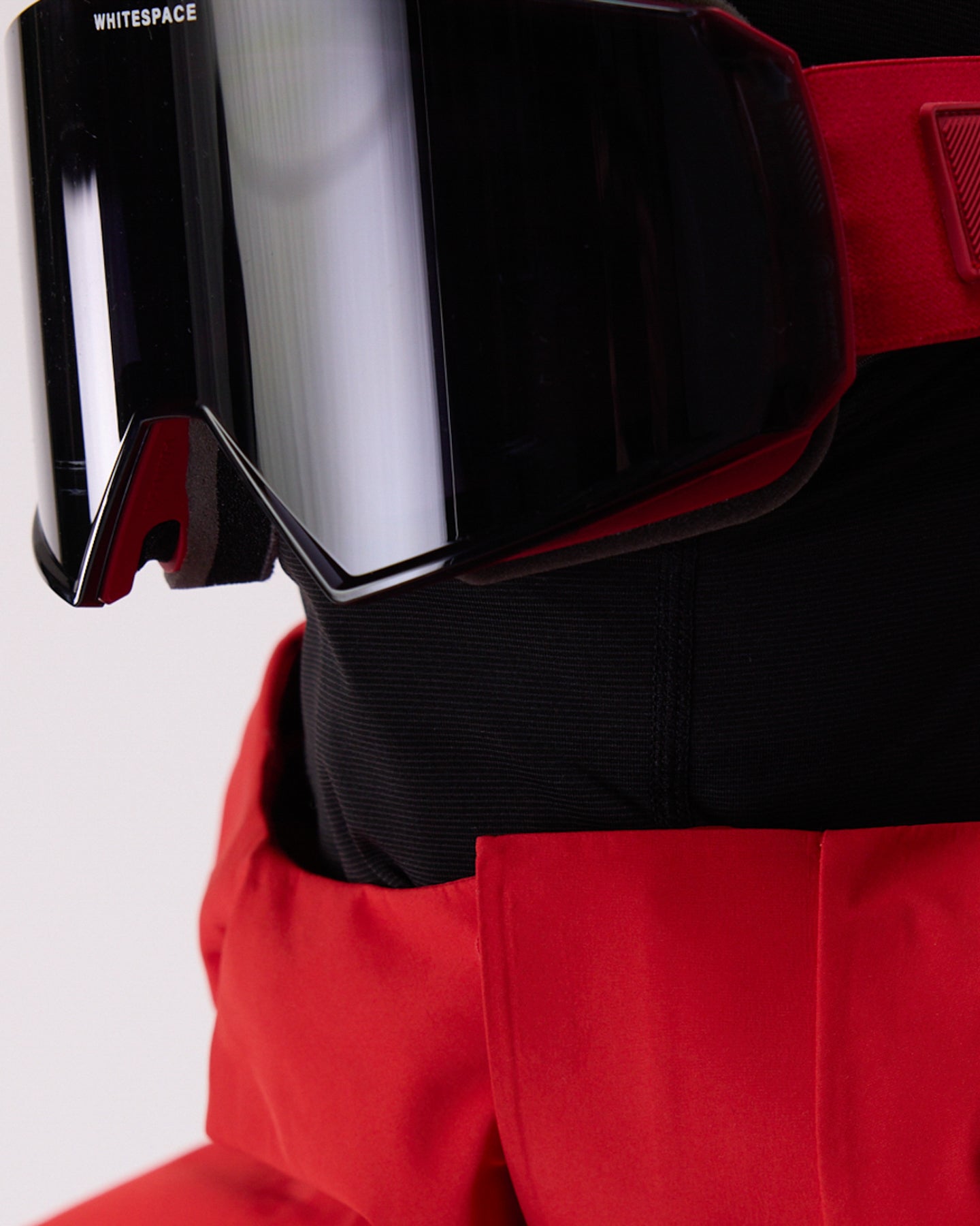 Close-up of a red and black ski outfit featuring WHITSPACE MD Icon Goggles with a reflective black lens. 