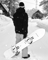 Person holding a snowboard with WHITESPACE branding in a snowy landscape with trees and houses in the background.