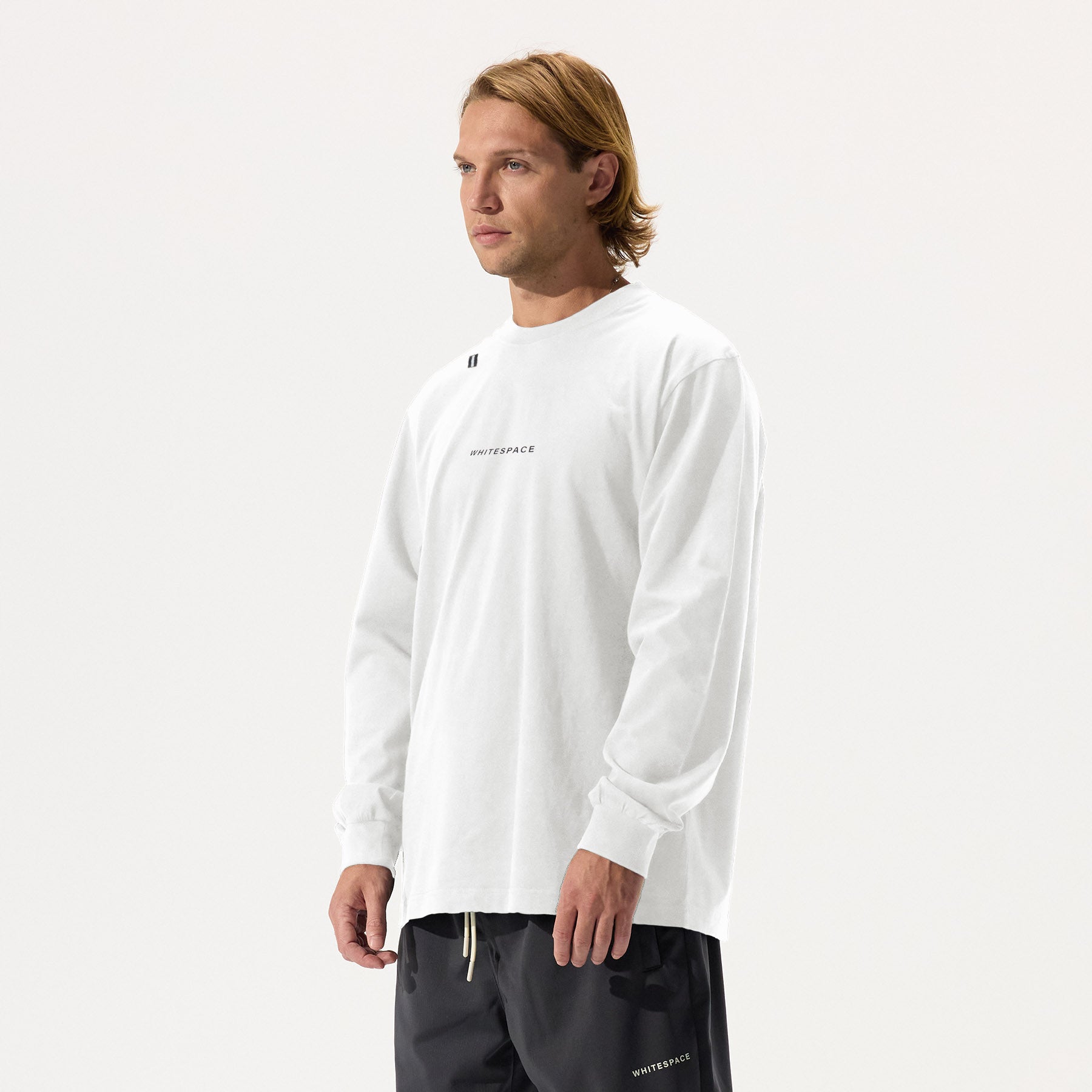 Model wearing a white long-sleeve shirt with WHITESPACE logo across the chest and black pants, on a white background