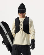 Model wearing WHITESPACE REC Cargo Vest in black over a cream shirt, black pants, black gloves, black beanie, and black ski goggle, holding a WHITESPACE snowboard under his arm, on a white background.