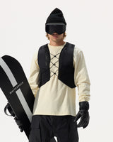 Model wearing WHITESPACE REC Cargo Vest in black over a cream shirt, black pants, black gloves, black beanie, and black ski goggle, holding a WHITESPACE snowboard under his arm, on a white background.