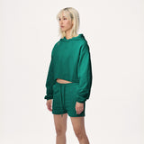 Model wearing WHITESPACE cropped hoodie in rainforest green and rainforest green sweatshorts, shown from the knees up, against a white background.
