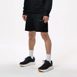 Model wearing WHITESPACE quarter zip sweatshirt in black and black fleece shorts with black shoes and white socks, shown from mid chest and down