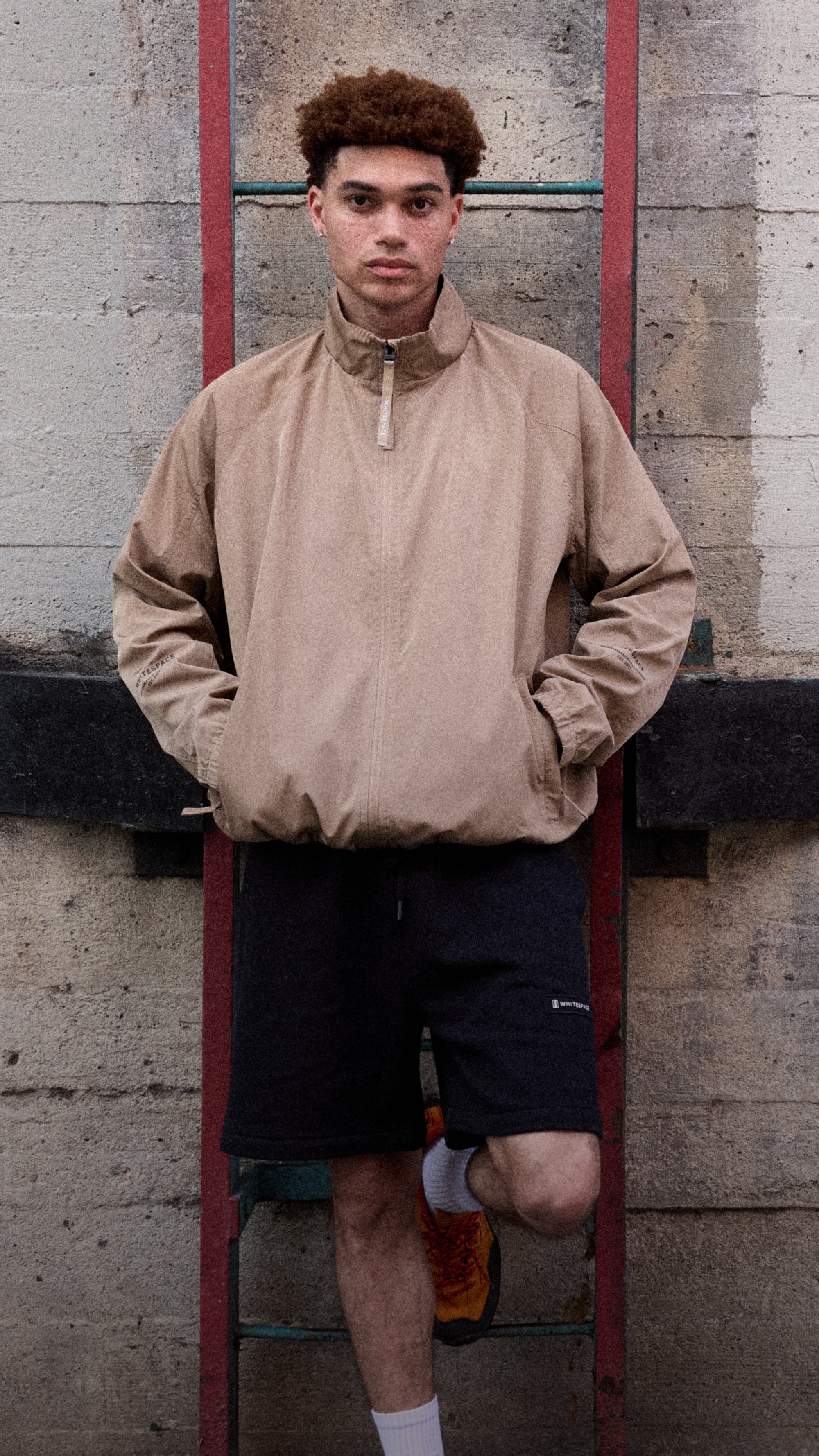 Model wearing the WHITESPACE Windbreaker Jacket in Desert Taupe and Fleece Shorts in Black.
