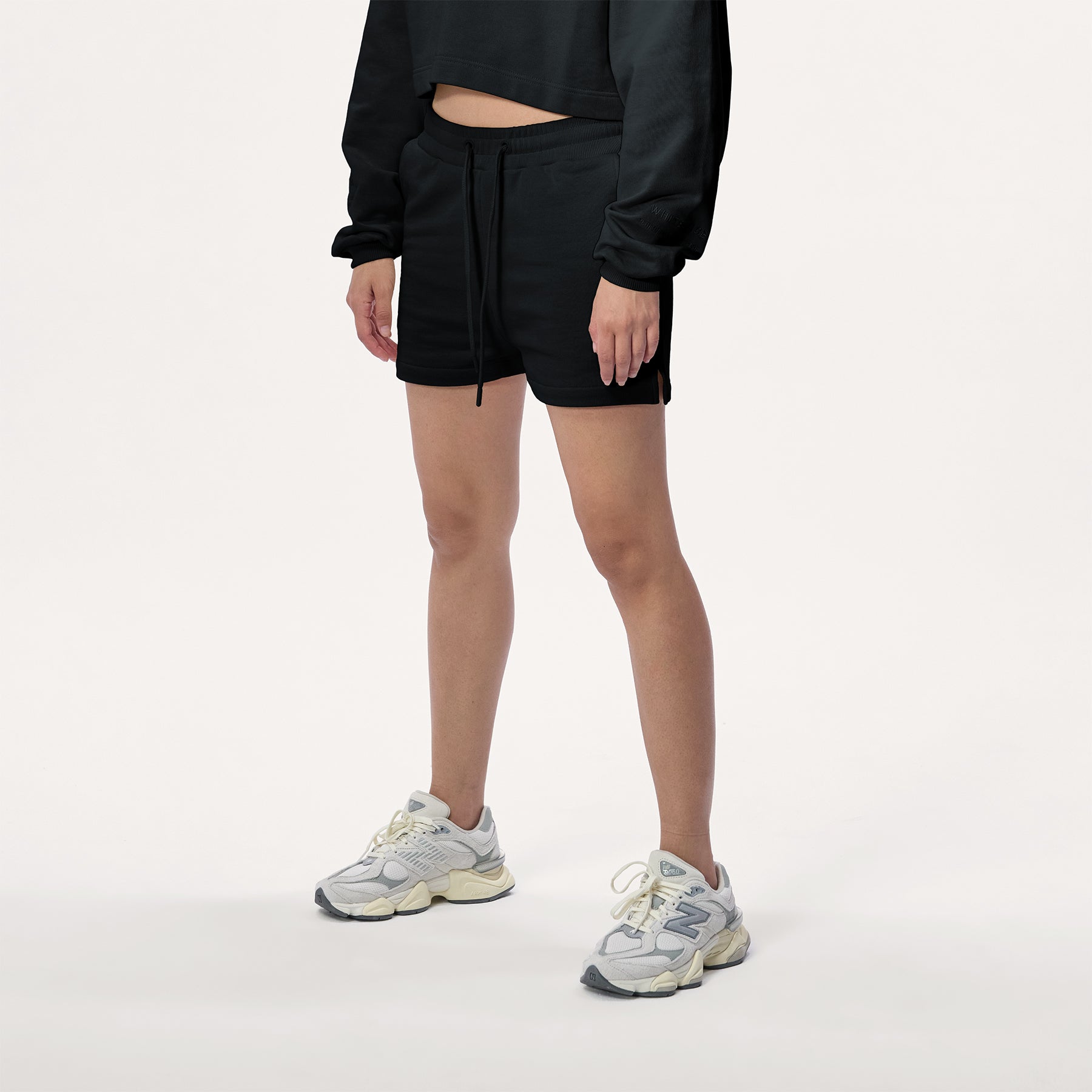 Model wearing WHITESPACE cropped hoodie in black and black sweatshorts with white shoes, shown from mid chest and down.