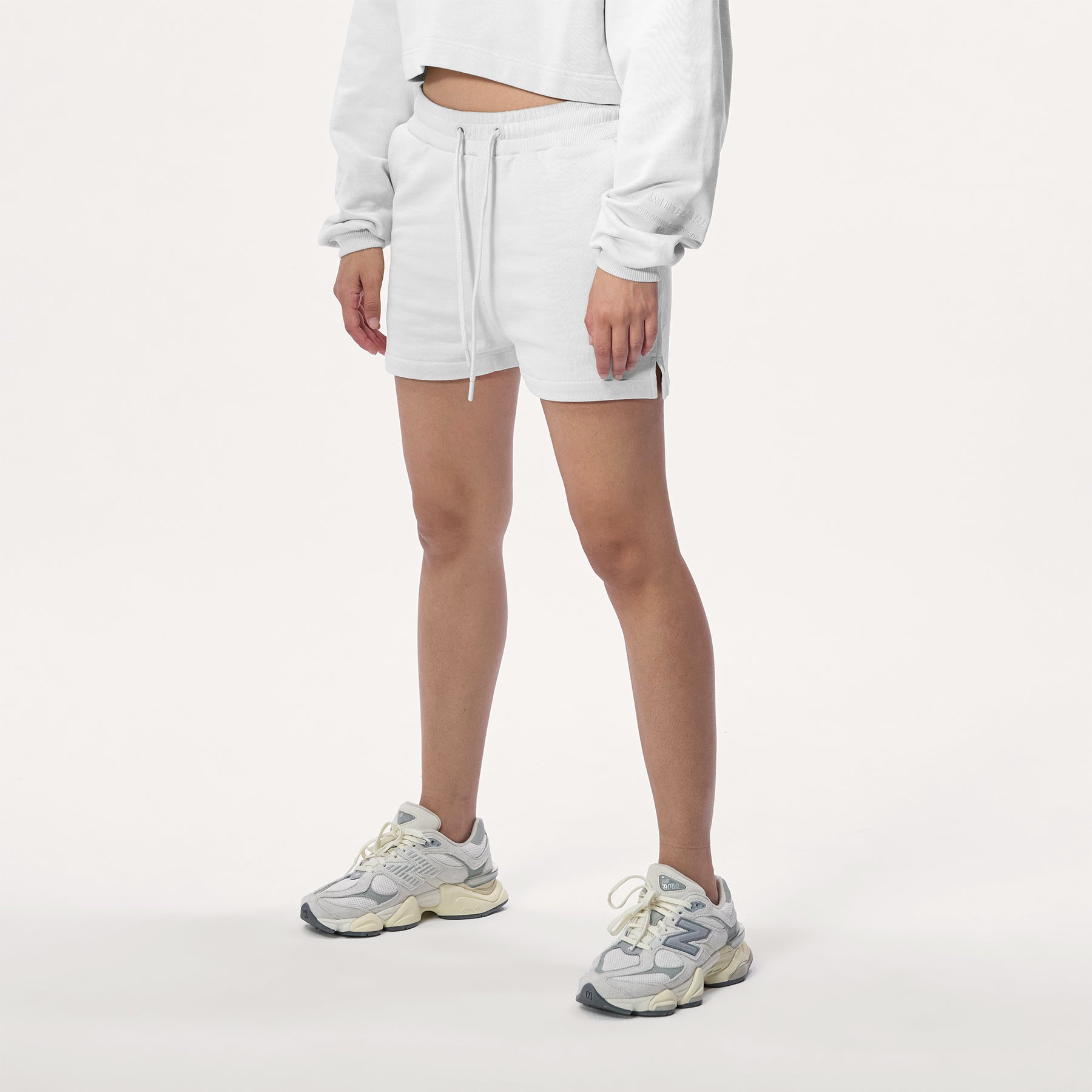 Model wearing WHITESPACE cropped hoodie in whisper white and whisper white sweatshorts with white shoes, shown from mid chest and down.