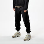 Model wearing WHITESPACE quarter zip sweatshirt in black and black WHITESPACE travel pants with light shoes and white socks, shown from mid chest and down