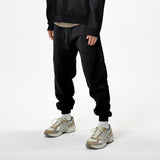 Model wearing WHITESPACE quarter zip sweatshirt in black and black WHITESPACE travel pants with light shoes and white socks, shown from mid chest and down