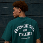 Model wearing a WHITESPACE rainforest green Premium Graphic SS tee against a dark wall.
