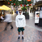 Man wearing a white WHITESPACE Unconventional Athletics hoodie and dark shorts on a city street