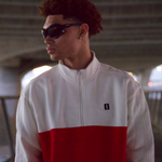 Man, shown from the chest up, standing under a bridge wearing WHITESPACE orange and white quarter zip and dark sunglasses.
