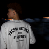Man, from the back, wearing a white WHITESPACE shirt with 'Unconventional Athletics' text, standing against a dark background.